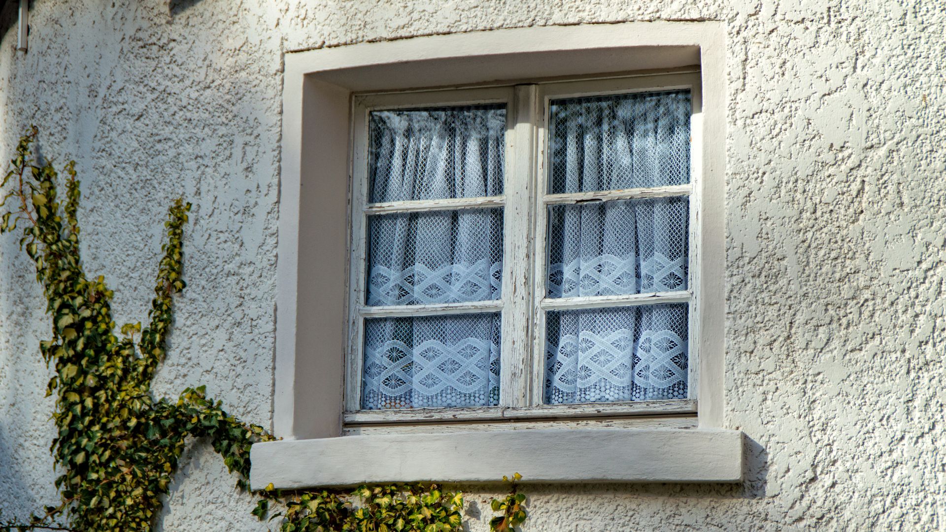A window with lace curtains on a textured wall.
