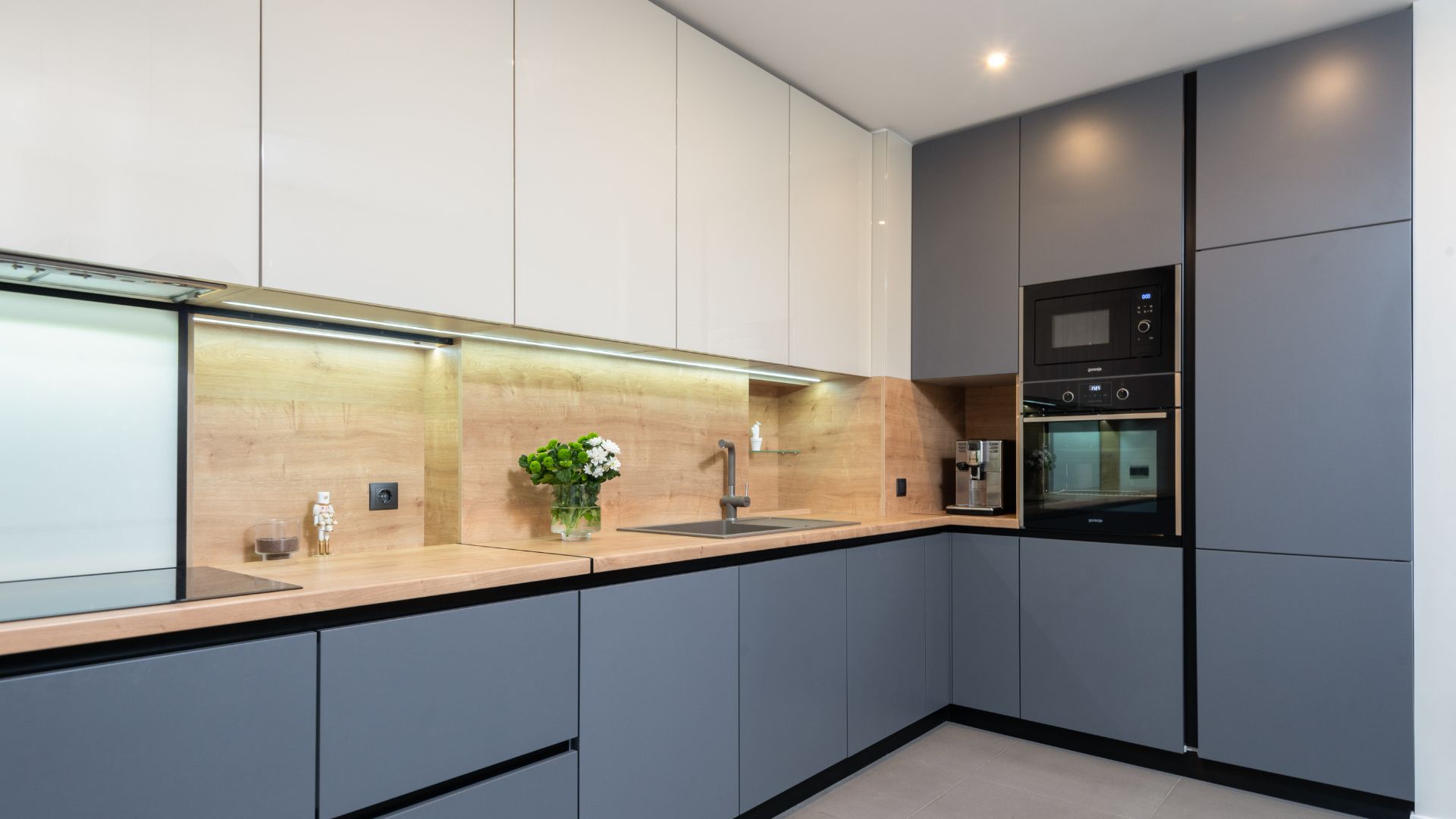 A modern kitchen with a combination of white and dark grey cabinets, wooden countertops, and built-in appliances.
