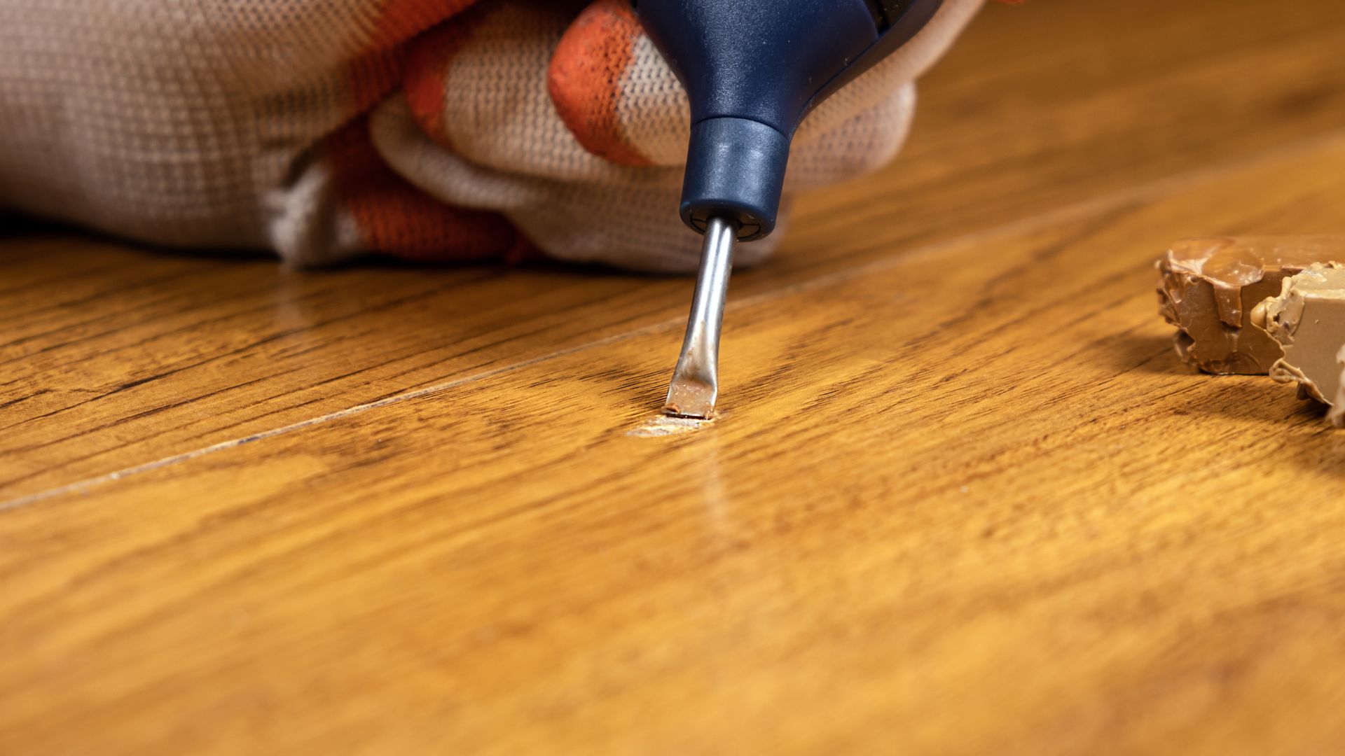 A close-up of a worker using a repair tool to fix a scratch on a wooden kitchen top.